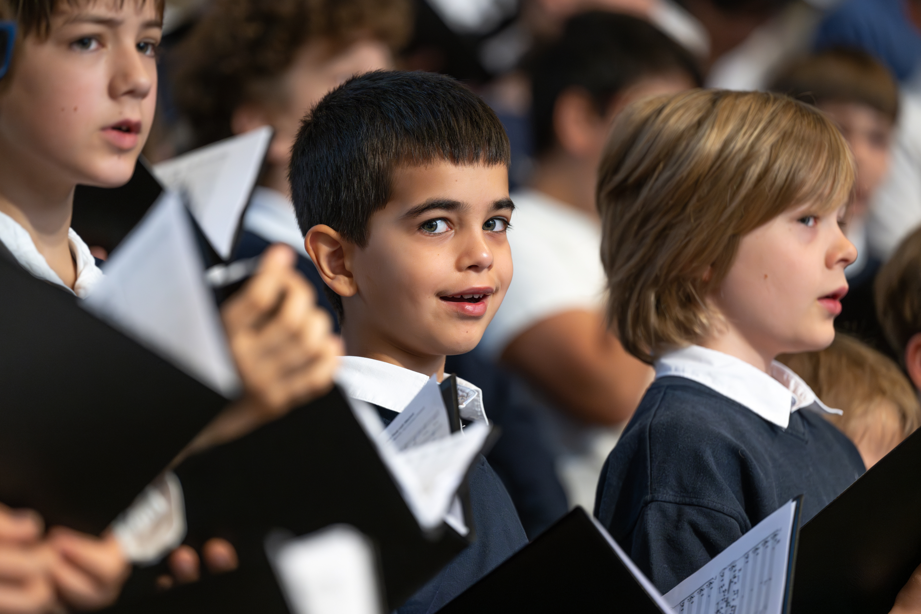 Kinderchor beim Konzert. Ein Junge grinst frech in die Kamera.