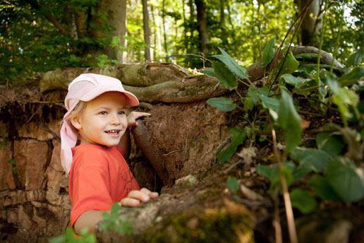 Ein Kind steht in einem Erdloch vor einer Wurzel im Wald