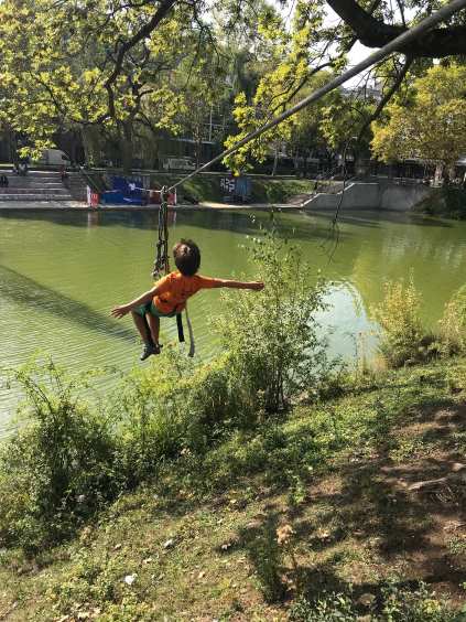 Kind das in einem Tragegeschirr hängt, mit dem es an einem Seil über Wasser rutscht