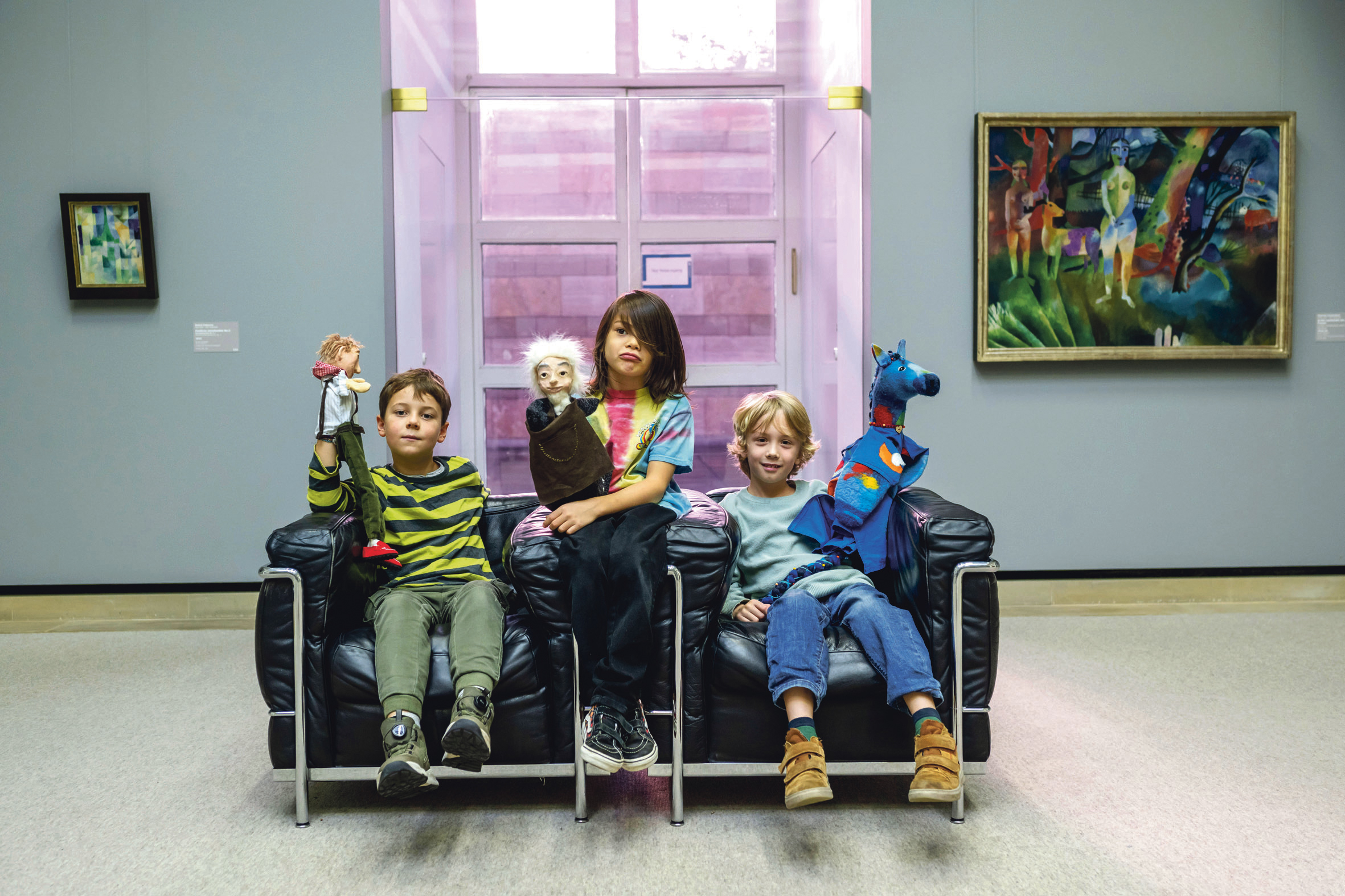 © Staatsgalerie Sander Pitl Zwei Kinder sitzen auf Ledersesseln und halten zwei Handpuppen in den Händen.