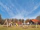 Ansicht aus der Ferne aus einen Spielplatz. Im Hintergrund sieht man mehrere Gebäude.