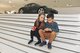 EIn Junge und ein Mädchen sitzen auf einer Treppe im Porschemuseum. Im Hintergrund sieht man Autos stehen.
