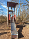 Spielturm mit einer Rutsche umgeben von Bäumen.