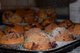 Ein Muffinblech mit frisch gebackenen Muffins ist zu sehen. Auf die Muffins wird gerade Puderzucker gestäubt.