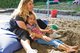 Frau und Mädchen sitzen zusammen in einem Sandkasten. Das Mädchen ist an die Frau gelehnt.