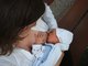Eine Mutter sitz mit einer weisen Bluse bekleidet und stillt ihr Baby.