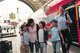 Eine Familie aus Vater, Mutter und drei Kindern steht lächelnd und Arm in Arm auf einem Bahnsteig neben einem roten Regionalzug mit geöffneten Türen
