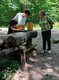 Zwei Jungen und eine ältere Frau stehen an einer Rätselstation im Wald.