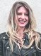 Das Bild zeigt die Journalistin und Autorin Laura Fröhlich. Sie trägt eine schwarze Lederjacke, ihre blonden Haare werden vom Wind verweht und sie lächelt.