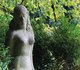 Eine aus Stein gehauene Statue steht vor grünen Büschen.