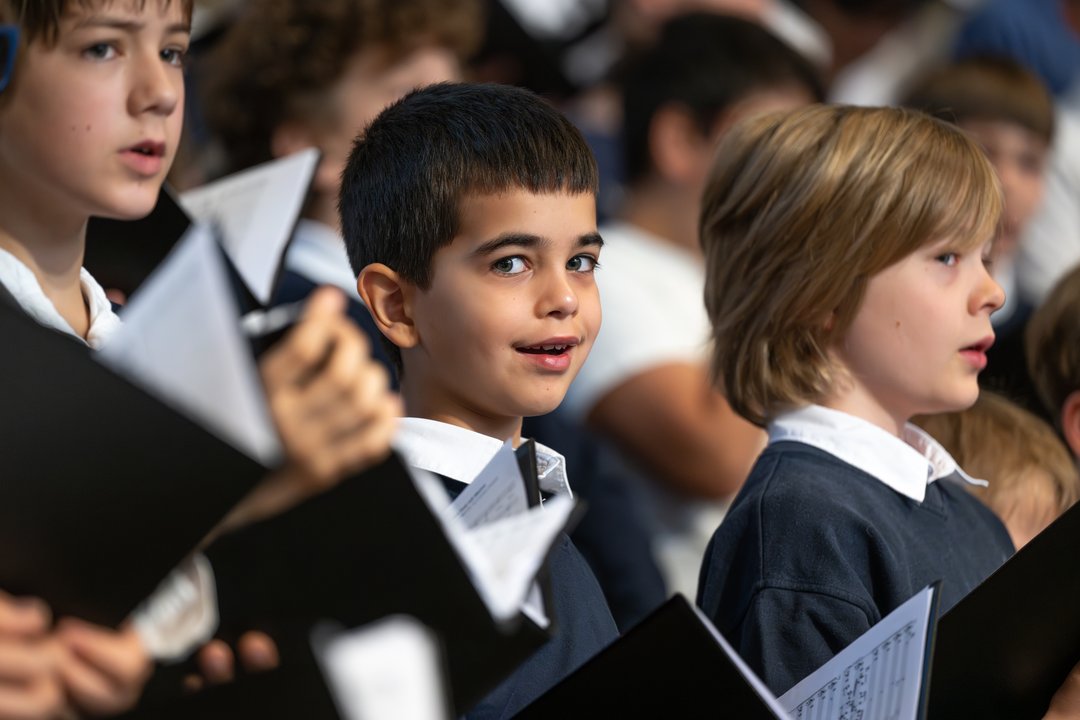 Kinderchor beim Konzert. Ein Junge grinst frech in die Kamera.