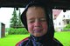 Ein kleiner Junge wurde mit zusammengekniffenen Augen und verzogenen Mund fotografiert. Er hat die Kapuze seiner Regenjacke über die hellblonden Haare gezogen.