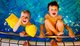 Zwei kleine Jungs halten sich am Rand eines Schwimmbeckens fest. Sie tragen Schwimmflügel.