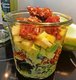 In einem Glas befindet sich ein geschichteter Salat. Ganz unten sind die Salatblätter, darüber Mango-Stücke und oben drauf liegen gegrillte Hühnchen-Stücke.