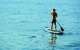 Ein Mann mit Badeshorts ist auf dem See beim Stand-Up-Paddling auf sehr ruhigem Wasser zu sehen.
