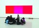 Mehrere Kinder sitzen im Kreis vor einer Erwachsenen bei einer Kinderführung im Schauwerk Sindelfingen, die Wand im Hintergrund ist weiß und auf ihr prangt ein großes Bild in drei verschiedenen Rot- und Pinktönen.